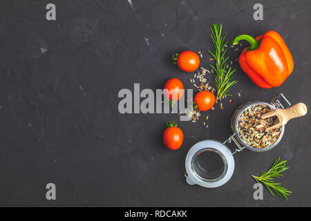 Schwarz, Violett, und weißer Reis (Oryza sativa) Mischung aus Glas Glas auf schwarzen Stein Beton texturierte Oberfläche Hintergrund. Rohe Paprika, Tomaten, Olivenöl und Stockfoto