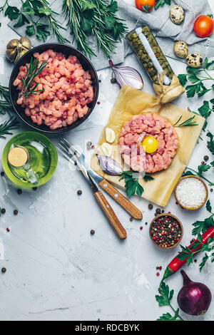 Gesundes Essen, kochen Konzept. Hausgemachte organischen Fleisch Hackfleisch und Tatar mit Eigelb mit Gemüse auf hellen grauen Stein Beton texturiert Stockfoto