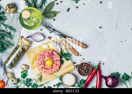 Steak Tartar mit Eigelb und Besteck Messer und Gabel auf hellen grauen Stein Beton texturierte Oberfläche Hintergrund mit Zutaten für die Herstellung. Kopieren s Stockfoto