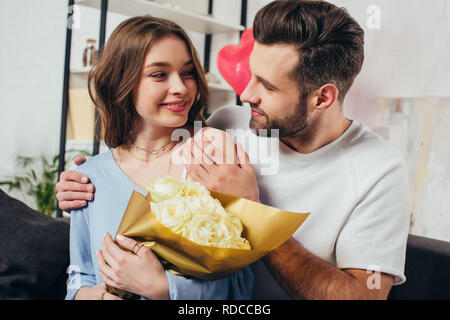 Glückliches Paar feiert Valentinstag Tag, während Jungen Mann umarmen Freundin mit Rosen Blumenstrauß Stockfoto