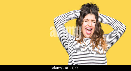 Junge schöne Frau mit Streifen Pullover verrückt und Angst mit den Händen am Kopf, Angst und überrascht von Schock mit offenen Mund Stockfoto