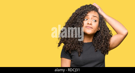 Junge schöne Frau mit lockigem Haar verwirren und um Frage wundern. Unsicher mit Zweifel, das Denken mit der Hand auf den Kopf. Nachdenkliches Konzept. Stockfoto