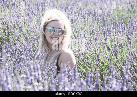 Portrait von Blond nach Frau steht in einem Lavendelfeld, lächelnd, in der Goldenen Stunde vor Sonnenuntergang in einem Lavendelfeld Stockfoto