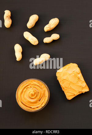 Schüssel mit Erdnussbutter, ohne schale Erdnüsse auf einem dunklen schwarzen Oberfläche, Ansicht von oben. Close-up. Stockfoto