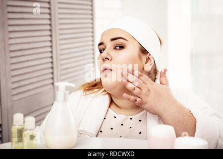 Konzentrierte Körper positive junge Dame, die Sahne auf ihrem Gesicht Stockfoto