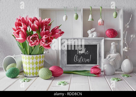 Frühling Hintergrund mit Ostern Dekorationen und eine Kreidetafel. Vitrine mit verschiedenen Objekten und rosa Tulpen. Text "Frohe Ostern" auf der bl Stockfoto