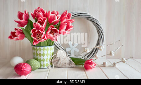 Frühling Arrangement mit Rosa gestreifte tulups, Ostereier, Holz- Herz und Gelbstirn-blatthühnchen Kranz auf hellen Hintergrund. Stockfoto