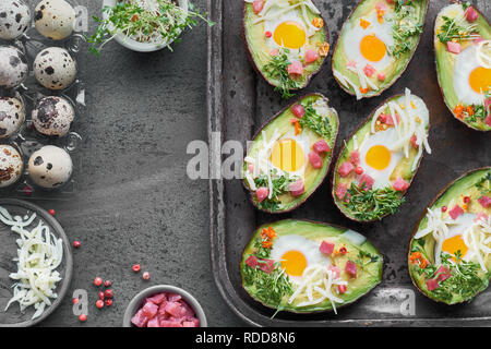 Keto Diät Teller: Avocado Boote mit Schinken würfeln, Wachteleier, Käse und Pfeffer in Backblech auf dunklem Hintergrund Stockfoto