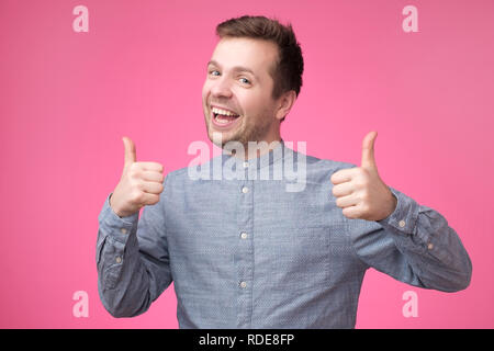 Jungen attraktiven Mann im blauen Shirt, Daumen oben gekleidet stehen über rosa Hintergrund Stockfoto