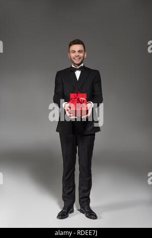 Schöne elegante Mann im schwarzen Smoking und Fliege gifting Rot auf Grau Stockfoto