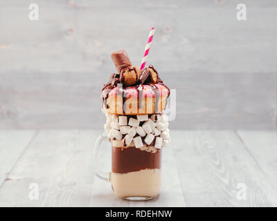 Schokolade Donuts und extreme Milchshake mit Marshmallow und andere Süßigkeiten in Mason jar auf grau Holz- Hintergrund. Crazy freakshake auf grau Holztisch Stockfoto