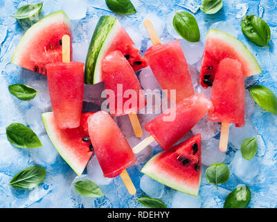 Blick von oben auf die Wassermelone und Basilikum Eis am Stiel auf blauem Hintergrund mit frischen grünen Blätter Basilikum und Wassermelone. Eis am Stiel Rezept Idee. Stockfoto