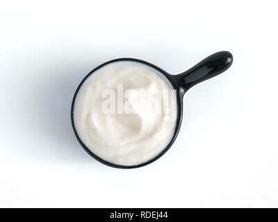Schönen griechischen Joghurt oder Sauerrahm in schwarz Schüssel, auf weißem Hintergrund mit Freistellungspfad isoliert. Ansicht von oben oder flach-legen. Stockfoto