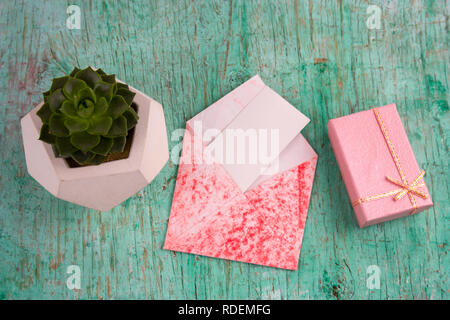 Ansicht von oben rosa Geschenk, saftigen potbox und Umschlag mit weißem Papier mock up schäbig Holz- Hintergrund Stockfoto