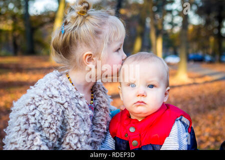Kaukasischen jungen Geschwister kiss außerhalb im Herbst und im Herbst mit Blättern Stockfoto