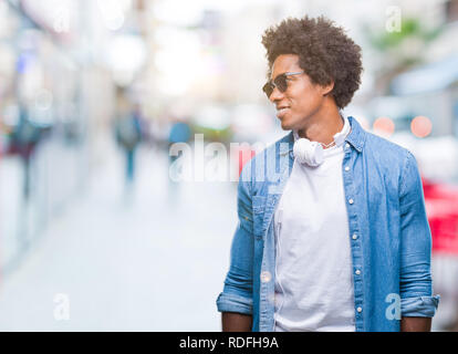 Afro-amerikanischer Mann mit Kopfhörern Musik hören über isolierte Hintergrund entfernt, mit einem Lächeln auf dem Gesicht zu Seite, natürlicher Ausdruck. Lachend Stockfoto