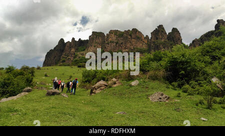 Freudige Reisende ist Spaß beim Wandern entlang der grünen Bergwiese auf dem Hintergrund der bewölkten Himmel. Gruppe der Wanderer zu Fuß auf den Felsen. Stockfoto