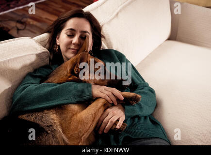 Schöne Portrait von lächelnden Frau ihren Hund Schäferhund zusammen umarmen vor dem Kamin in der gemütlichen Wohnung im Winter Tag in Glück Freundschaft Stockfoto