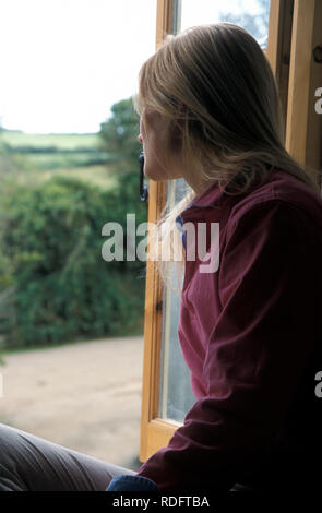 Unglückliche junge Frau aus Schlafzimmer Fenster über ländliche Landschaft Stockfoto