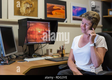 Dame in home office lächelnd, während auf dem Mobiltelefon Stockfoto
