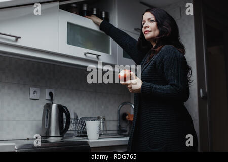 Schöne brünette Frau mit einem Apfel in der Küche Stockfoto