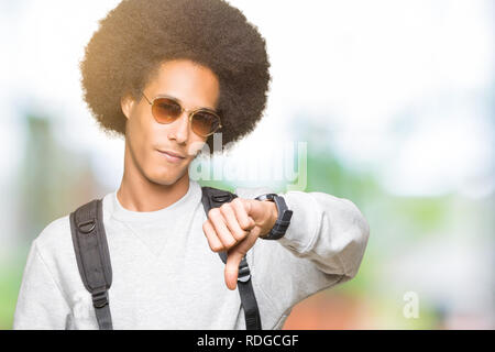 Junge afrikanische amerikanische Mann mit afro Haar mit Sonnenbrille und Rucksack mit Verärgerten Gesicht, negatives Vorzeichen zeigen Abneigung mit Daumen nach unten, Ablehnung c Stockfoto