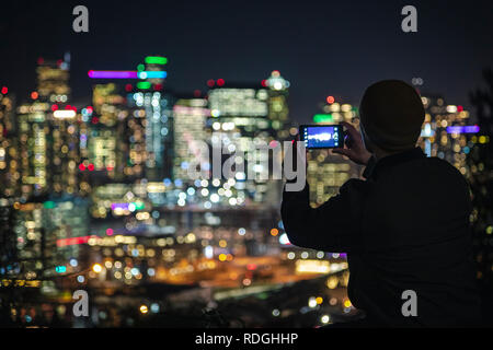 Bunte verschwommenen Hintergrund aus städtischen Gebäude bei Nacht mit Mann hält Handy mehrere Fotos für soziale Medien Stockfoto