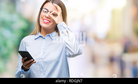 Junge schöne Geschäftsfrau SMS-Nachricht mit dem Smartphone über isolierte Hintergrund mit glücklichen Gesicht lächelnd tun ok Zeichen mit der Hand auf Auge lookin Stockfoto