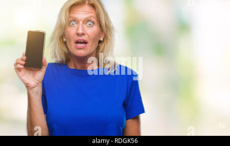 Blonde Frau mittleren Alters mit leerer Bildschirm des Smartphones über isolierte Hintergrund im Schlag mit einer Überraschung konfrontiert, ängstlich und aufgeregt mit Angst Angst Stockfoto