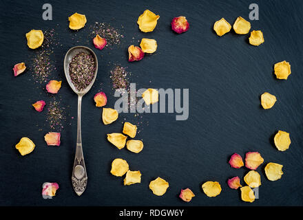 Blumen Tee in einem silbernen Löffel, und Rosenblättern Rahmen auf schwarzem Schiefer Hintergrund. Stockfoto