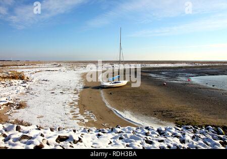 Bucht im Wattenmeer mit einem Segelboot, verschneite Strand auf der ostfriesischen Nordseeinsel Spiekeroog, Niedersachsen Stockfoto