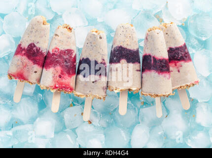 Hausgemachtes Eis Popsicle mit Beeren, Müsli und Chia Samen. Gesund Sommer Frühstück Konzept. Eis am Stiel aus Joghurt und Banane mit Beeren und Müsli. Ansicht von oben. Copyspace Stockfoto