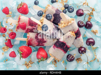 Selbstgemachte popsicle, Kirsche, Heidelbeere, Erdbeere, Himbeere. Gesund Sommer Frühstück Konzept. Eis am Stiel aus Joghurt und Banane mit Beeren, Müsli und Chia Samen. Ansicht von oben. Stockfoto
