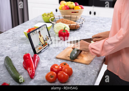 Frau Schneiden von Gemüse auf Schneidebrett Vor der digitalen Tablet auf den Küchentisch Stockfoto