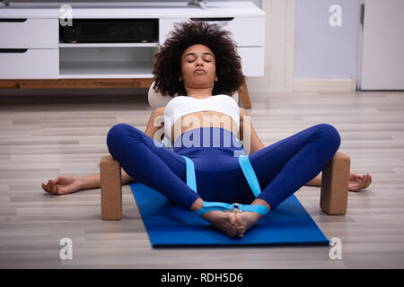 Entspannt junge Frau liegend auf Fitness Matte, Übung mit Yoga Gürtel und zwei Blöcke Stockfoto