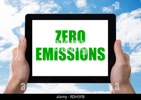 Des Menschen Hand Digital Tablet mit Null Emissionen Text auf dem Bildschirm gegen bewölkter Himmel Stockfoto