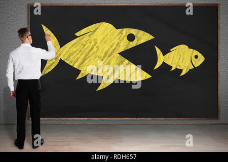 Rückansicht eines Geschäftsmannes Zeichnung Skizze der grosse Fische fressen Kleine Fische auf der Tafel Stockfoto