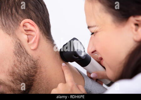 Nahaufnahme einer jungen Ärztin Kontrolle der Haut am Hals des Mannes mit Dermatoskop Stockfoto