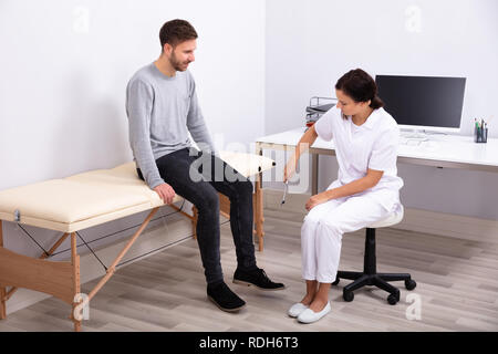 Junge weibliche Arzt prüfen Knie Reflexe der männlichen Patienten mit Reflexhammer Stockfoto