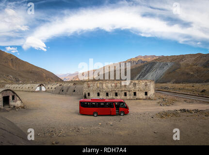 Ein roter Bus in Las Cascaras alte Ruinen aus dem Bau von Quebrada El Jao Damm am Cajon del Maipo, Chile Stockfoto