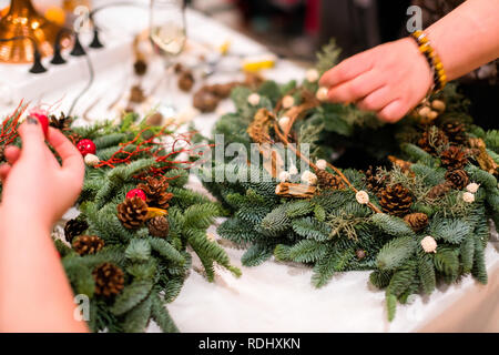 Weihnachten Kranz Weberei. Frau Hände verzieren holiday Wreath der Fichte Äste, Kegel und verschiedenen organischen Dekorationen auf dem Tisch Stockfoto