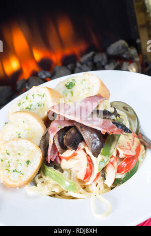 Pasta Carbonara mit Linguini, Pilz und Paprika mit Speck garniert und serviert mit in Scheiben geschnittenen Knoblauch Baguette Stockfoto