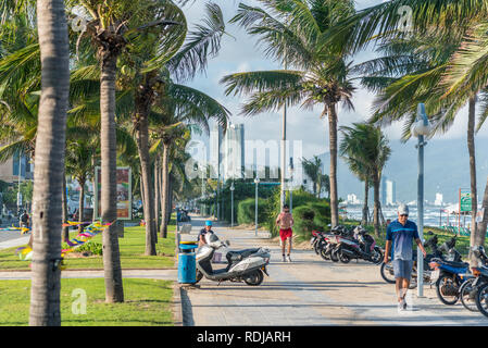 Da Nang, Vietnam: der Gehweg der Straße am Meer (Vo Nguyen Giap) entlang My-khe Strand mit Palmen im Wind, Leute sitzen, Gehen, Joggen und das Meer. Stockfoto