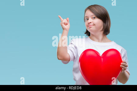 Junge erwachsene Frau mit Down Syndrom halten roten Herzen über isolierte Hintergrund sehr zufrieden zeigt mit Finger- und an der Seite Stockfoto