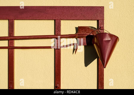 Rote Feuerwehrmann Schild mit Spaten Haken und einem Kegel aus Sand auf einem hellen, sonnigen Tag auf dem Hintergrund der Gelbe rauhe Wände Stockfoto