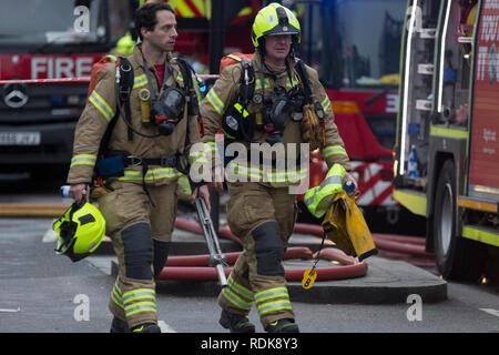 Feuerwehrleute sorgen sich ein Brand in den Räumlichkeiten auf der Walworth Road, am 16. Januar 2019 in London, England. Nach Londoner Feuerwehr, "Zehn Löschfahrzeuge und rund 70 Feuerwehrmänner wurden zu einem Brand in einem Shop mit Wohnungen oben auf der Walworth Road in Walworth genannt. Im Erdgeschoss des Gebäudes durch die Flamme und einen kleinen Teil des Untergeschosses zerstört wurde, im ersten Stock und im zweiten Stock wurden auch beschädigt. Feuerwehrmänner tragen von Atemschutzgeräten gerettet ein Mann und eine Frau aus dem ersten Stock Flachdach mit einer Schiebeleiter. Die Frau wurde an der Szene für Rauch einatmen dann Tak behandelt Stockfoto