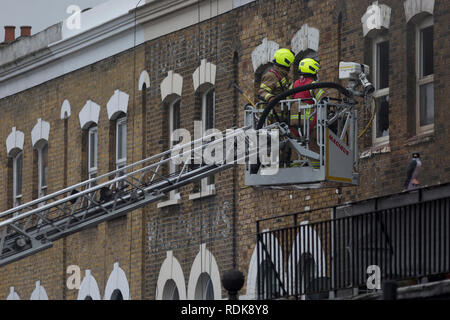 Feuerwehrleute sorgen sich ein Brand in den Räumlichkeiten auf der Walworth Road, am 16. Januar 2019 in London, England. Nach Londoner Feuerwehr, "Zehn Löschfahrzeuge und rund 70 Feuerwehrmänner wurden zu einem Brand in einem Shop mit Wohnungen oben auf der Walworth Road in Walworth genannt. Im Erdgeschoss des Gebäudes durch die Flamme und einen kleinen Teil des Untergeschosses zerstört wurde, im ersten Stock und im zweiten Stock wurden auch beschädigt. Feuerwehrmänner tragen von Atemschutzgeräten gerettet ein Mann und eine Frau aus dem ersten Stock Flachdach mit einer Schiebeleiter. Die Frau wurde an der Szene für Rauch einatmen dann Tak behandelt Stockfoto