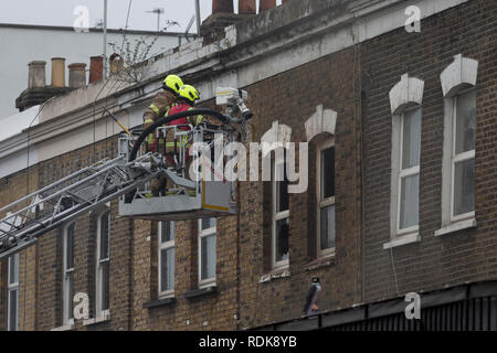 Feuerwehrleute sorgen sich ein Brand in den Räumlichkeiten auf der Walworth Road, am 16. Januar 2019 in London, England. Nach Londoner Feuerwehr, "Zehn Löschfahrzeuge und rund 70 Feuerwehrmänner wurden zu einem Brand in einem Shop mit Wohnungen oben auf der Walworth Road in Walworth genannt. Im Erdgeschoss des Gebäudes durch die Flamme und einen kleinen Teil des Untergeschosses zerstört wurde, im ersten Stock und im zweiten Stock wurden auch beschädigt. Feuerwehrmänner tragen von Atemschutzgeräten gerettet ein Mann und eine Frau aus dem ersten Stock Flachdach mit einer Schiebeleiter. Die Frau wurde an der Szene für Rauch einatmen dann Tak behandelt Stockfoto