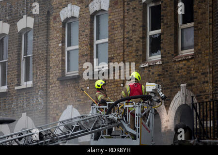 Feuerwehrleute sorgen sich ein Brand in den Räumlichkeiten auf der Walworth Road, am 16. Januar 2019 in London, England. Nach Londoner Feuerwehr, "Zehn Löschfahrzeuge und rund 70 Feuerwehrmänner wurden zu einem Brand in einem Shop mit Wohnungen oben auf der Walworth Road in Walworth genannt. Im Erdgeschoss des Gebäudes durch die Flamme und einen kleinen Teil des Untergeschosses zerstört wurde, im ersten Stock und im zweiten Stock wurden auch beschädigt. Feuerwehrmänner tragen von Atemschutzgeräten gerettet ein Mann und eine Frau aus dem ersten Stock Flachdach mit einer Schiebeleiter. Die Frau wurde an der Szene für Rauch einatmen dann Tak behandelt Stockfoto