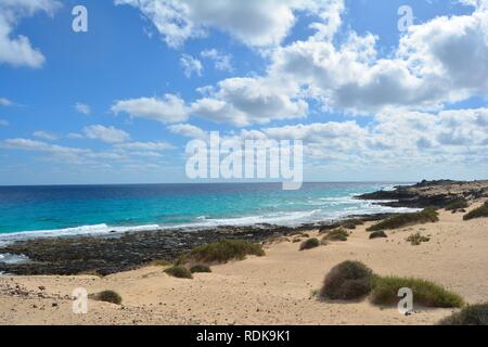 Wüste Küste von Corralejo, Fuerteventura, Spanien. Naturpark Dünen. Türkisfarbene Meer und bewölkt blauer Himmel. Stockfoto